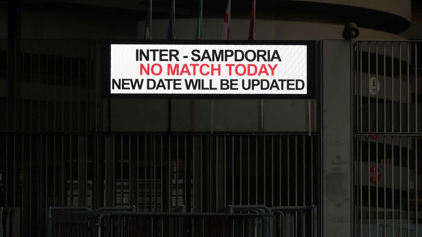 A white sign with red and black writing is attached to a darkened concrete stadium.