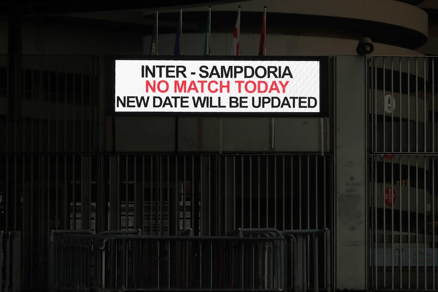 A white sign with red and black writing is attached to a darkened concrete stadium.