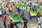 People marching through a street carrying green, yellow, and blue flags