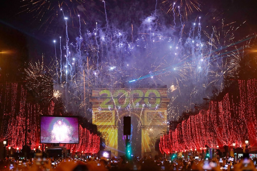 Revellers photograph coloured fireworks exploding over the Arc de Triomphe.