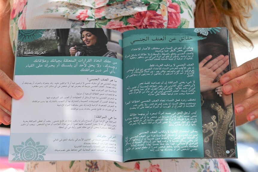A woman holding open a green and white paged booklet with arabic writing