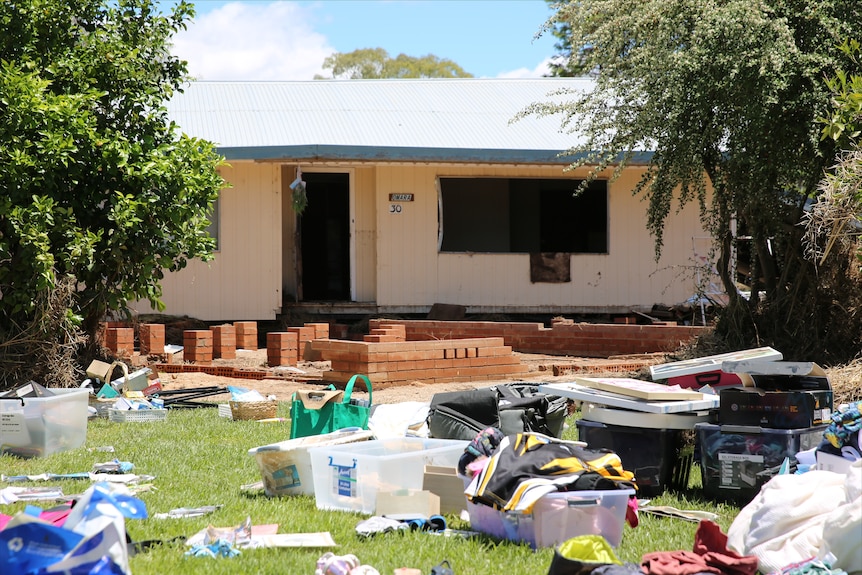 Lawn covered in household items and rubbish. foundations of a home exposed with a home in the background