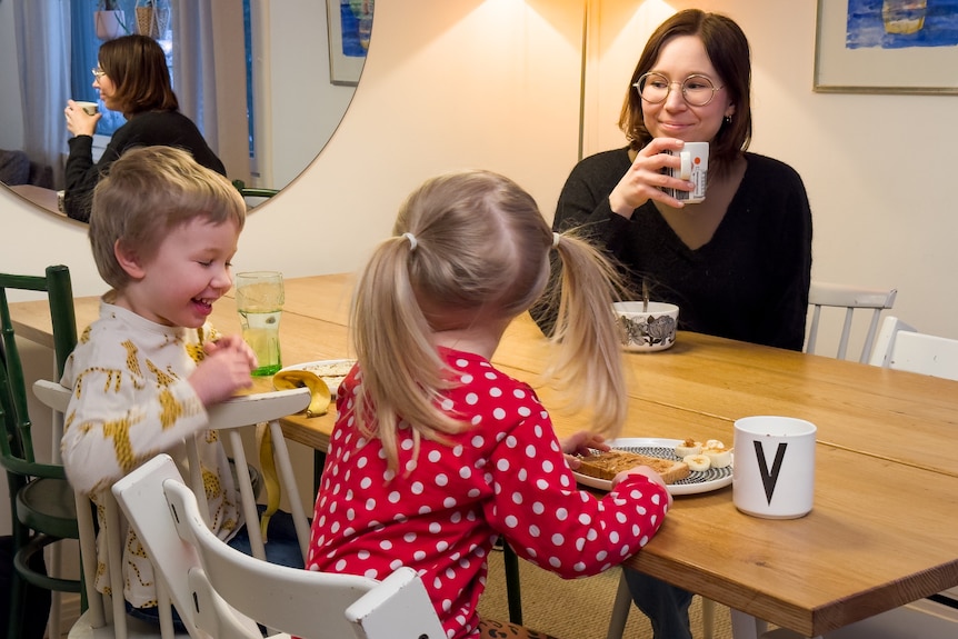 A woman sitting at a dining table with her young son and daughter eating breakfast.