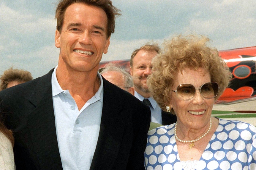 A photo of a man in a shirt and jacket next to an older woman with sunglasses and curly hair. 