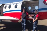 A man and a woman stand outside a Royal Flying Doctor Service plane, wearing blue and red shirts.