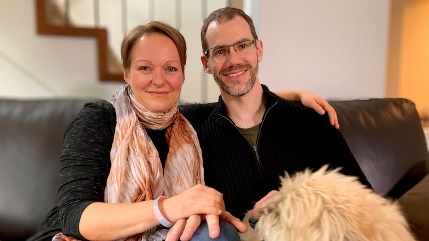 A woman and a man wearing glasses sitting with a dog on their laps.