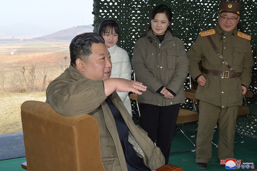 Kim Jong Un sits speaking as his wife, daughter and a military officer look on. 