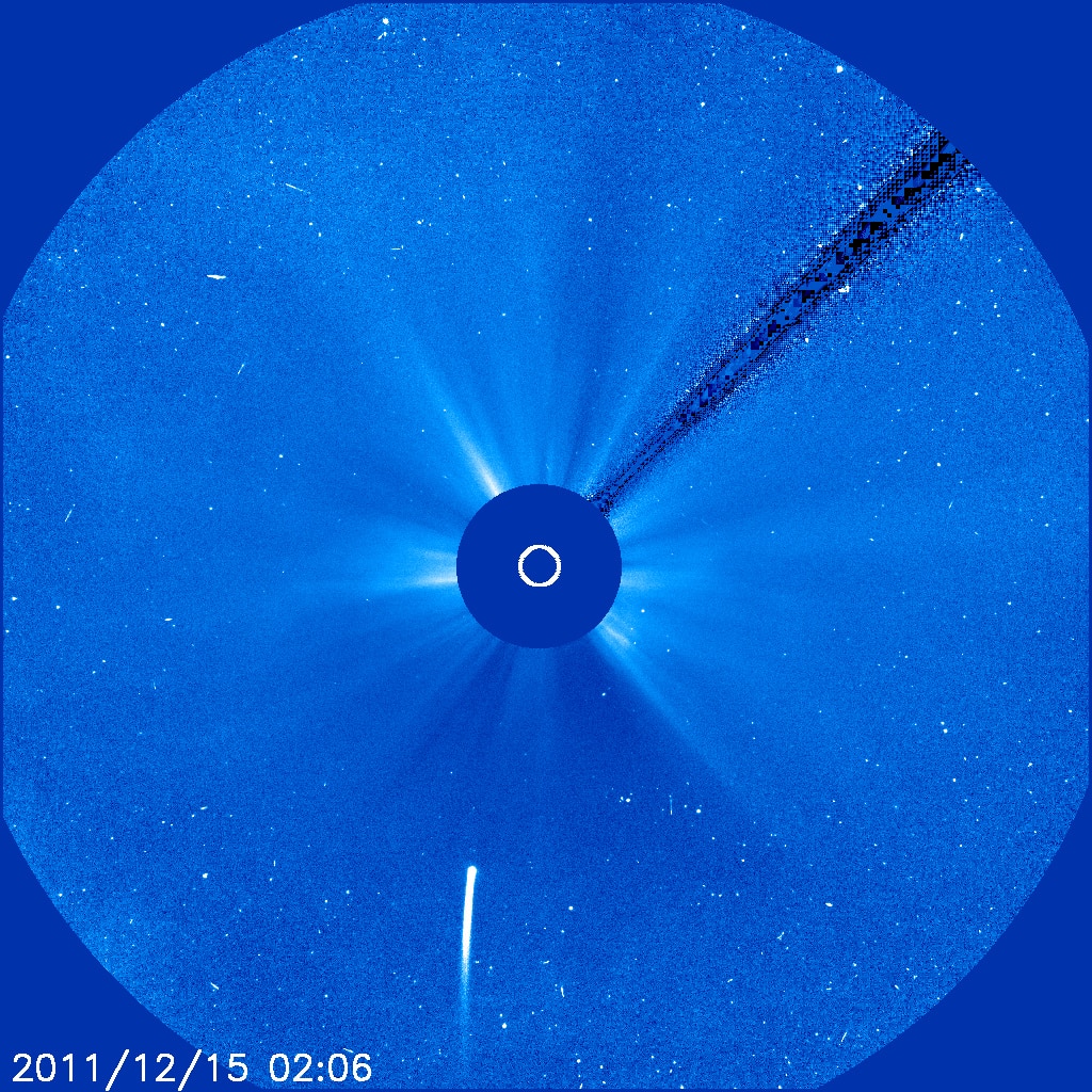 Blue image of a starfield, with a bright object in the middle blocked out and a comet approaching from the bottom.