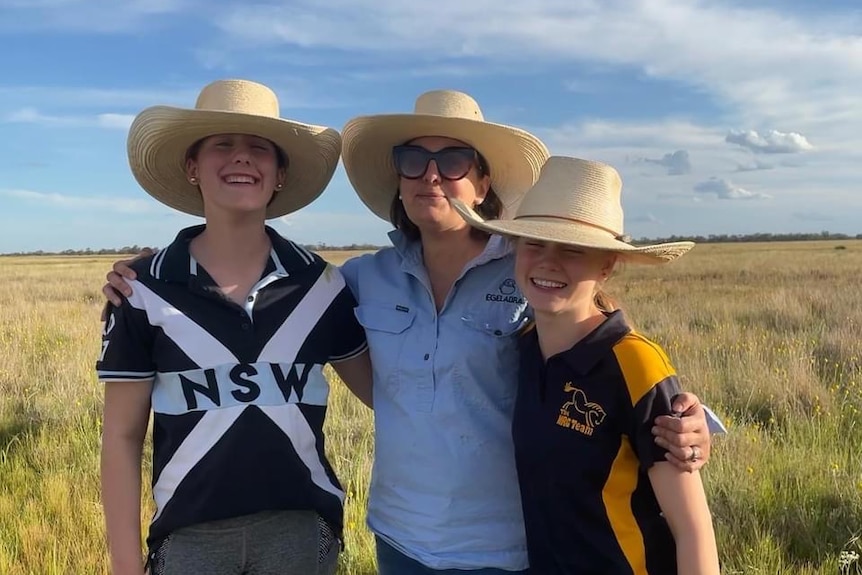 A woman and two girls in a field wearing hats