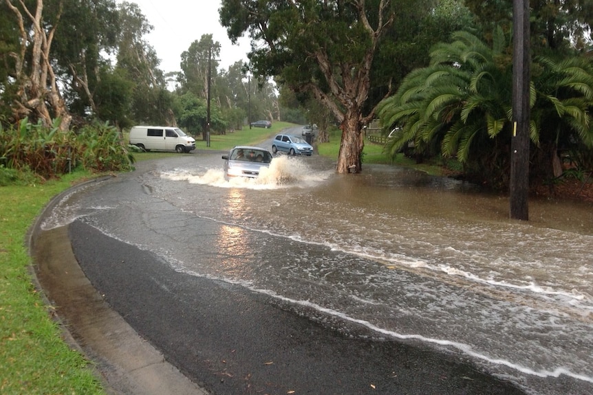 A car drives through flood waters on a road near Wollongong.