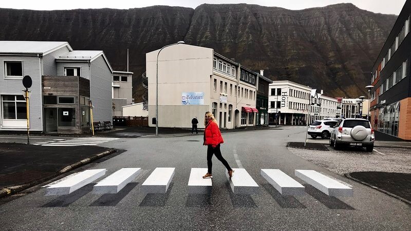 Woman in red puffer jacket walks across three dimensional zebra crossing in Iceland