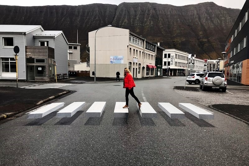 Woman in red puffer jacket walks across three dimensional zebra crossing in Iceland