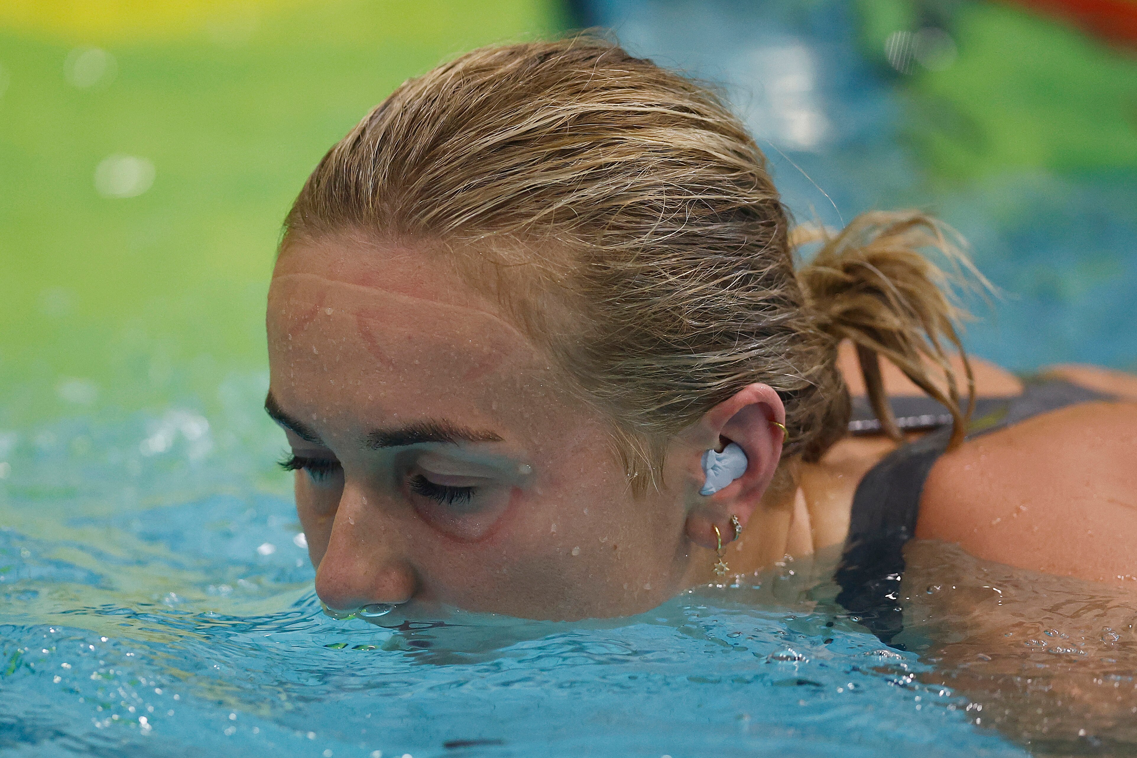 Ariarne Titmus closes her eyes and has her mouth in water with an ear plug in her ear
