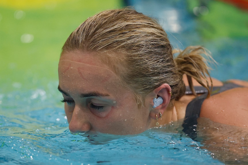 Ariarne Titmus closes her eyes and has her mouth in water with an ear plug in her ear