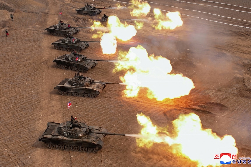 A view from above showing military tanks in a row participating in a demonstration and bright orange flames coming from them.