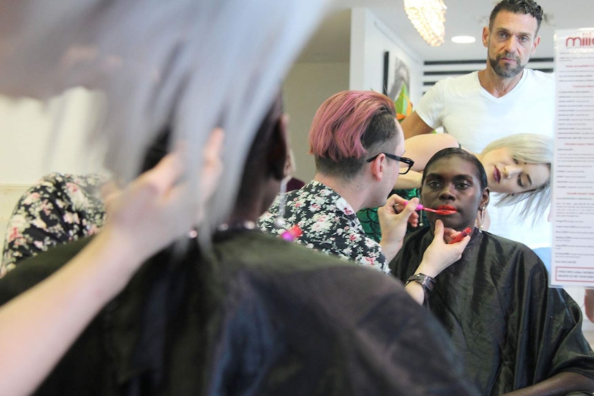 a woman getting her makeup done as people watch on