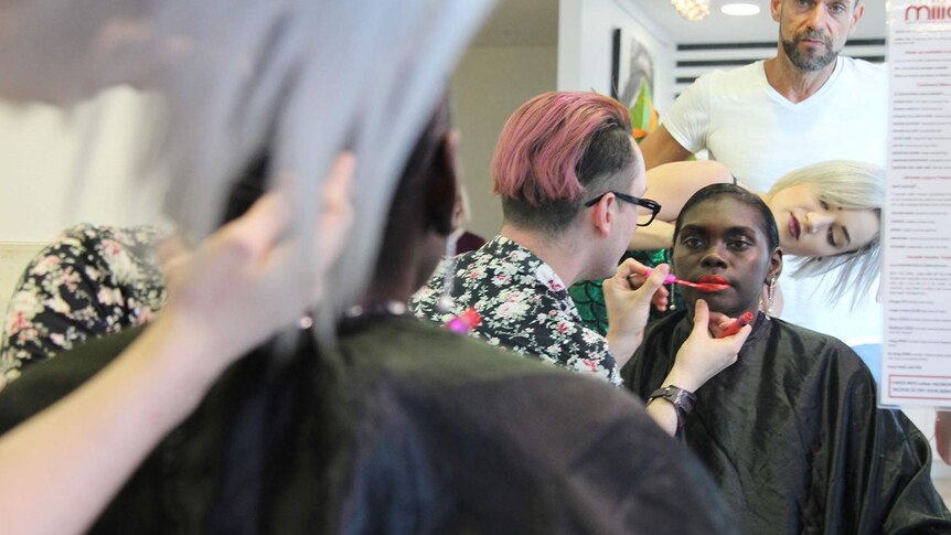 a woman getting her makeup done as people watch on