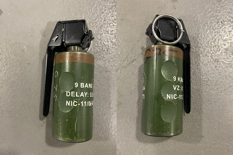 A small green canister with a black clip and metal pin. 