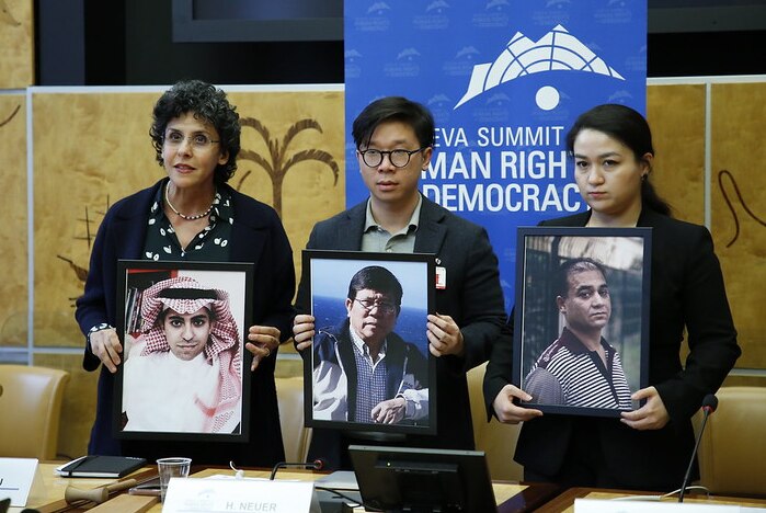 Two women and a man stand holding portraits of political prisoners.