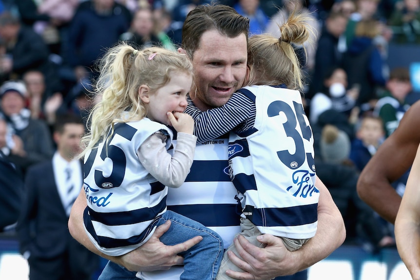 A Geelong AFL player holds his two daughters before a match.