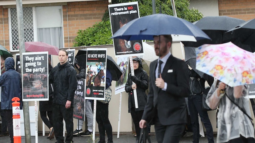 Derby Day racegoers walk past protesters.