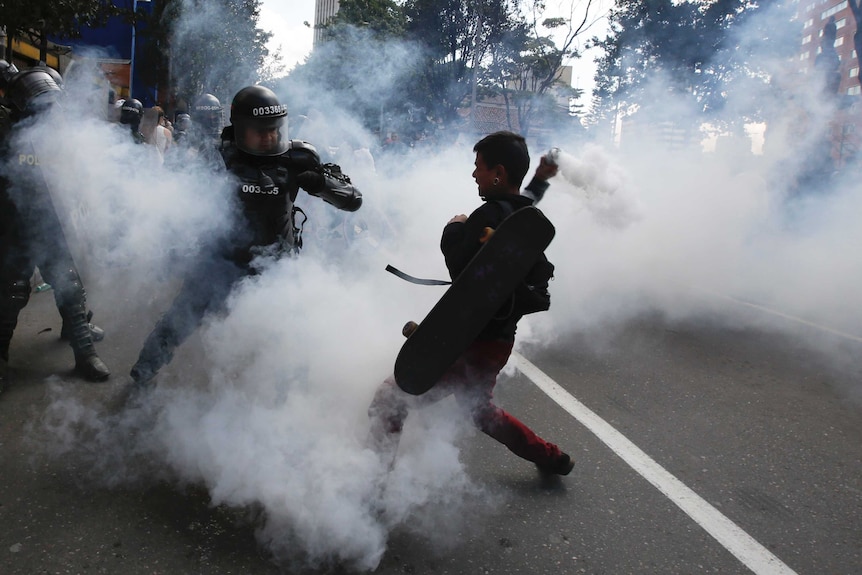 Police and protestor clash amid smoke on the street in Bogota