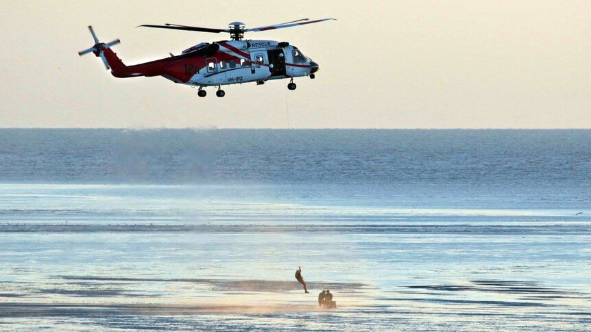 A helicopter is used to winch two men to safety.