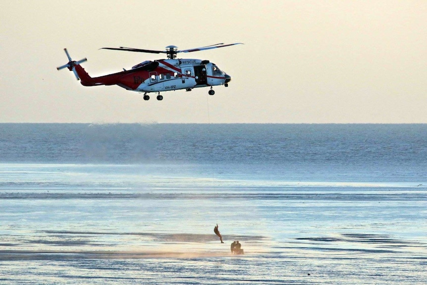 A helicopter is used to winch two men to safety.