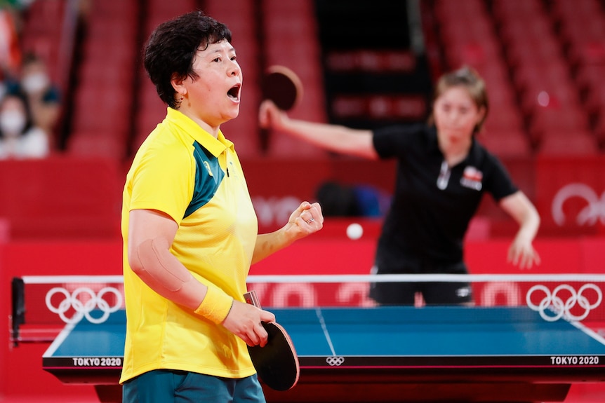 A brunette woman wearing a yellow shirt clenches her fist