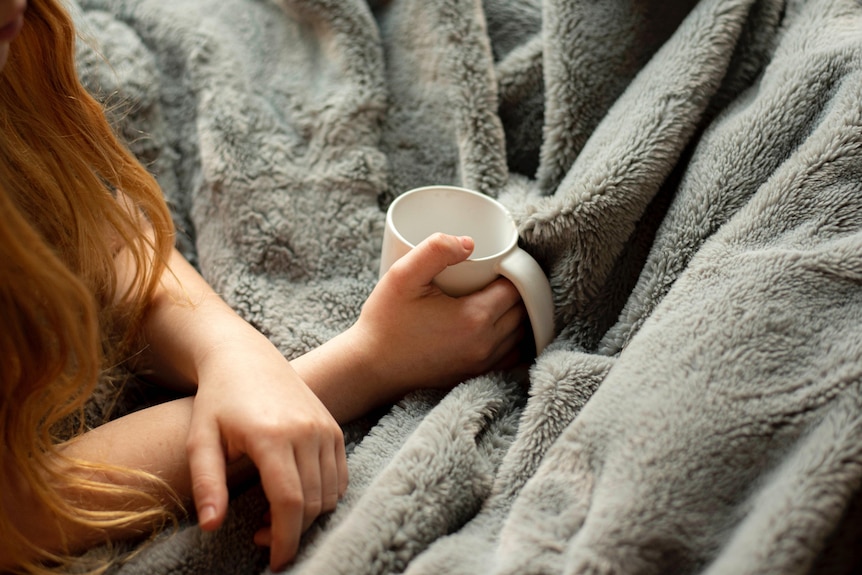 Birdseye view of two female hands holding a mug, close of of hands and mug resting on a fluffy blanket.