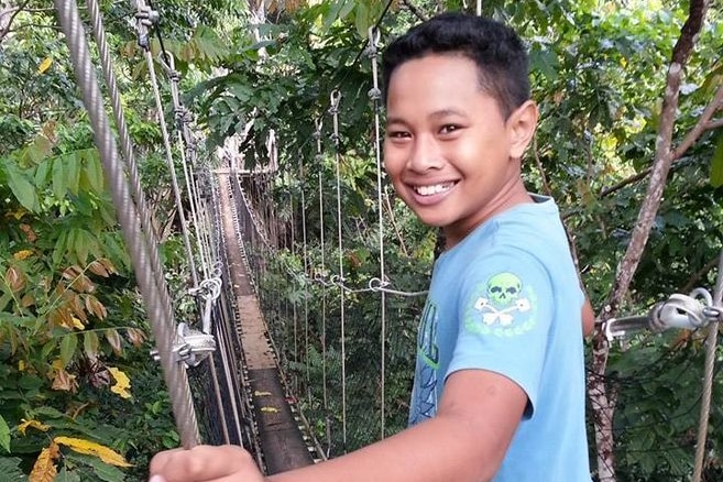 A smiling young boy stands among rainforest treetops on a suspended bridge