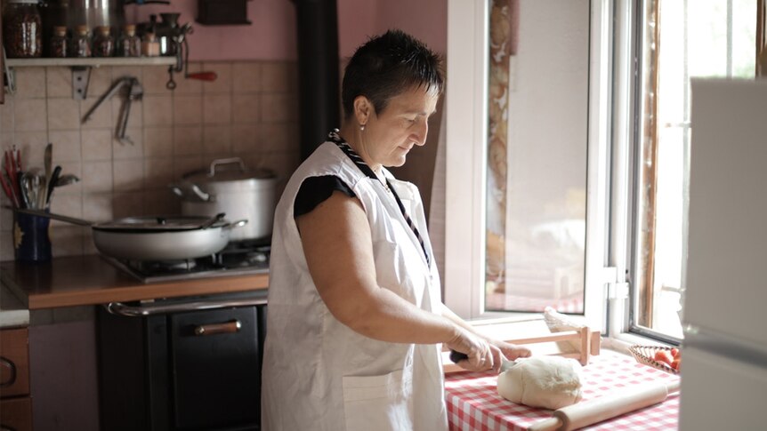 A woman kneads bread dough in front of a kitchen window