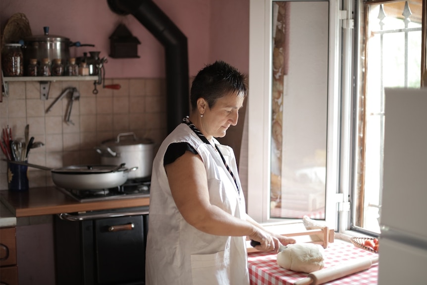 A woman kneads bread dough in front of a kitchen window