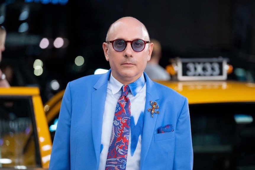 Willie Garson, dressed as Standford Blatch in a blue suit, looks at the camera with a serious expression.
