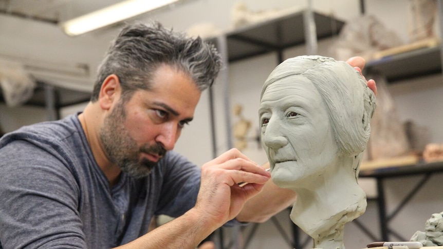 An artist works on a sculpture of a human face.