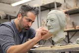 An artist works on a sculpture of a human face.