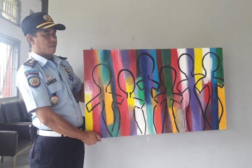 A prison guard holds a colourful painting