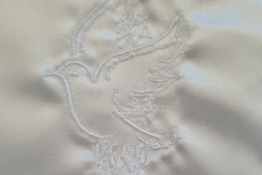 An embroidered dove in white cotton on white satin.