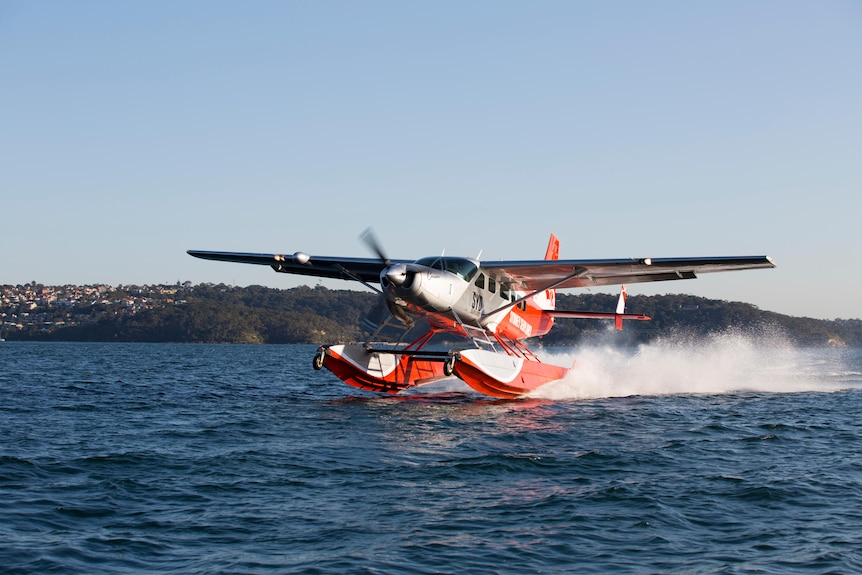 An orange and grey seaplane landing on water. 