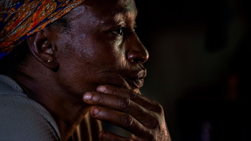 An African woman sits with her hand on her chin and stares ahead 