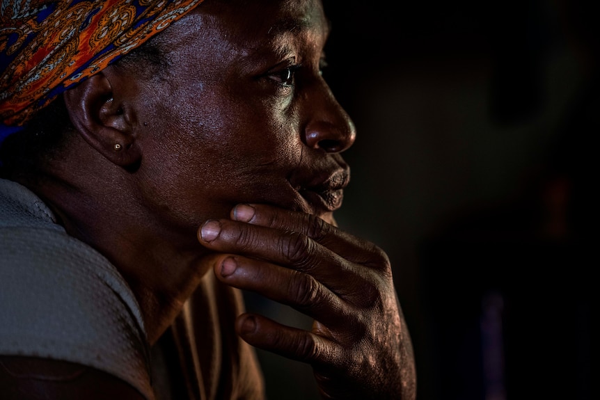 An African woman sits with her hand on her chin and stares ahead 