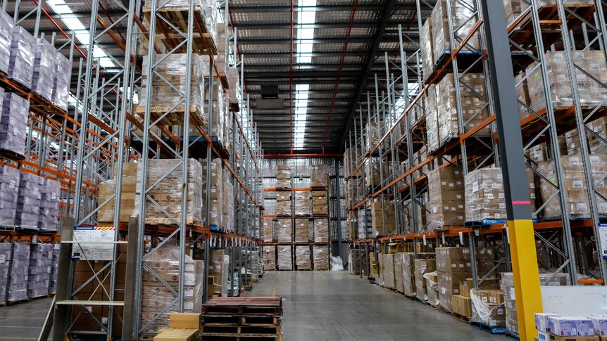 Large concrete floor warehouse with rows of boxes of medical equipment stacked high beneath a silver padded roof