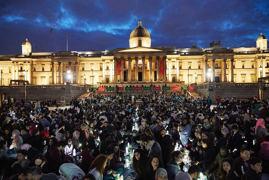 A crowd of people enjoying meals after sunset on a lawn