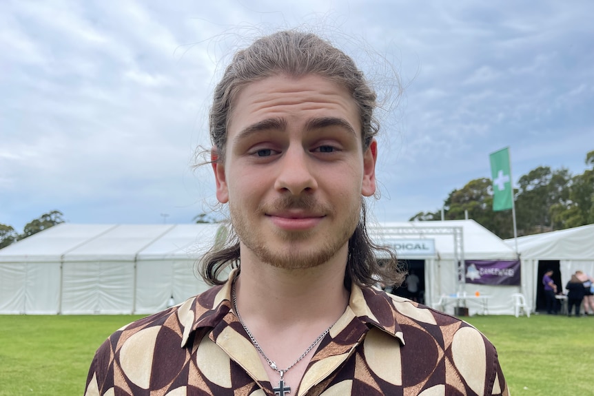 Young male with tied back brunette hair squinting towards camera.