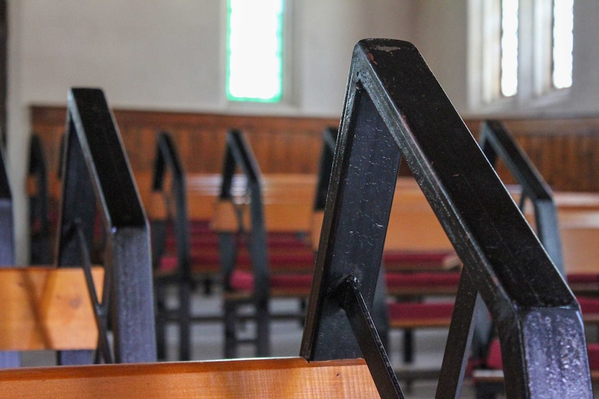 Wooden church pews with red, velvet cushions.