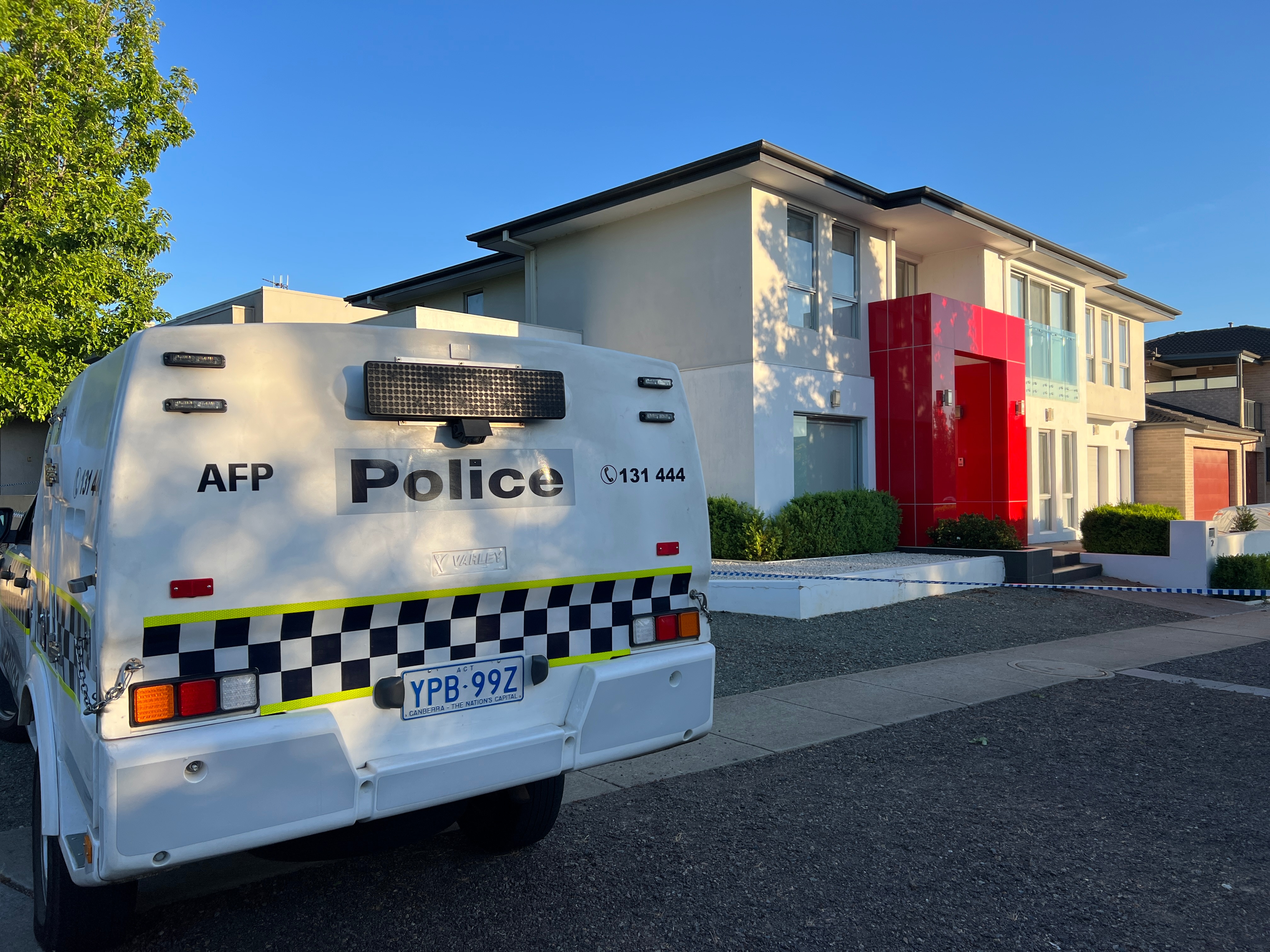 The back of a white and blue police car beside a two-story house with a red door. 