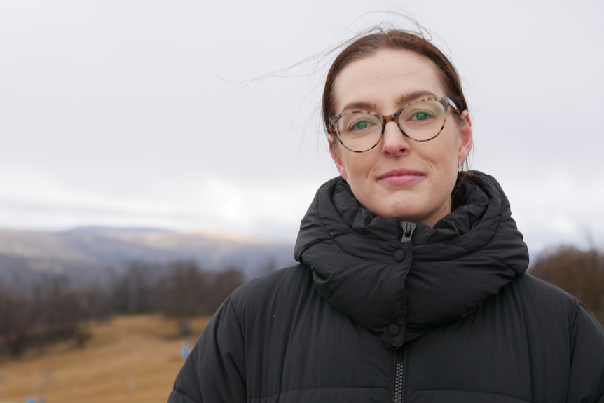 a woman smiles at the camera with the slopes in the background