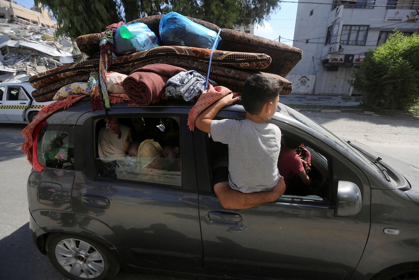 A child sitting on a car loaded with packages.