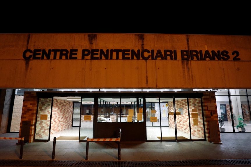 Exterior de un edificio de hormigón con puertas de cristal y un cartel encima. 