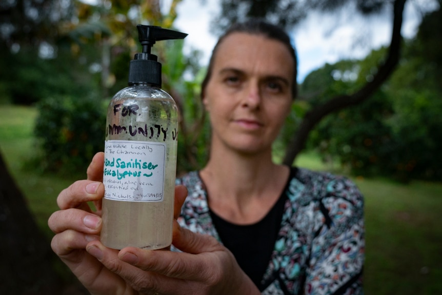 A woman holds up a small pump bottle labelled as hand sanitiser for community use.
